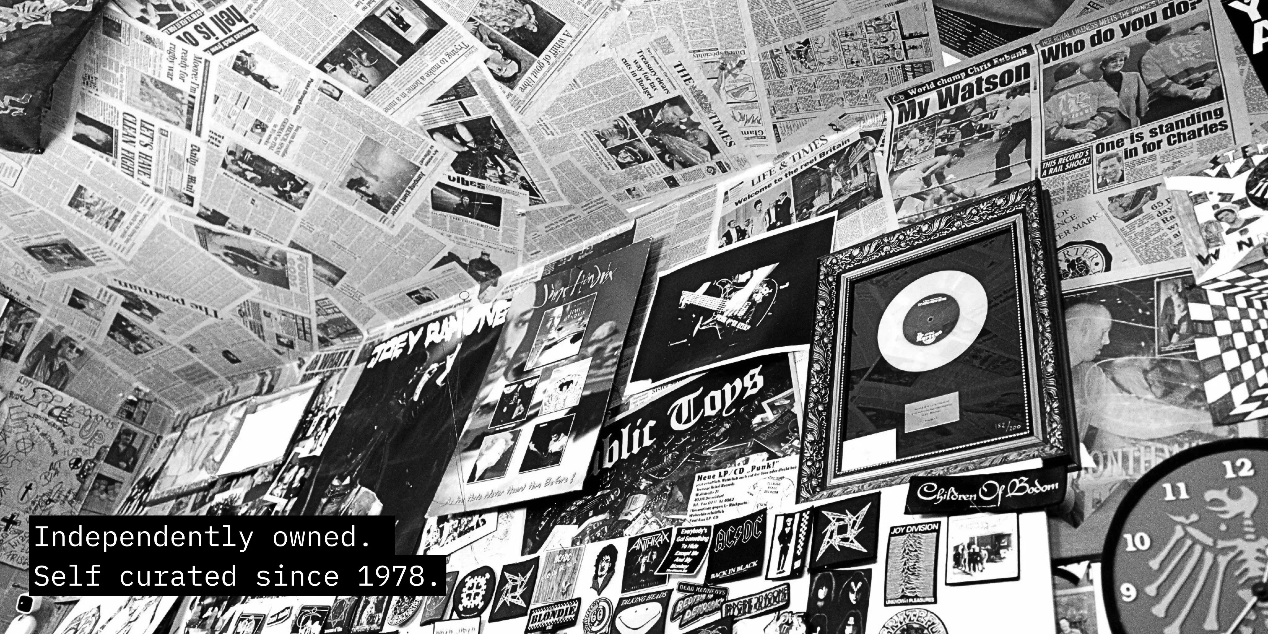 Interior wall of Pick Up Düsseldorf featuring punk records, newspapers and subculture memorabilia, photographed in black and white.